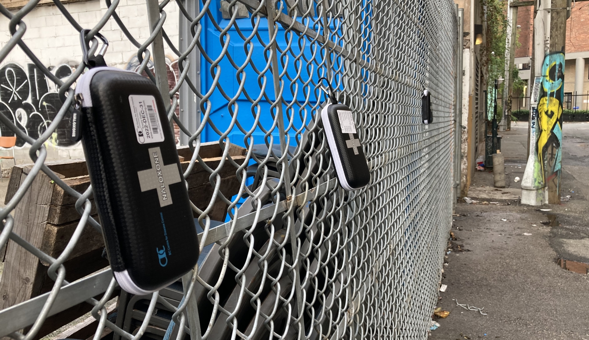 A narcan kit hanging on a chain link fence
